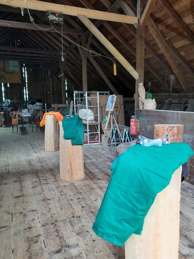 Vorbereitete Holzstämme stehen auf Arbeitsplätzen in der Scheune von Andreas Patzak, jeder Stamm mit Schnittschutzkleidung.
