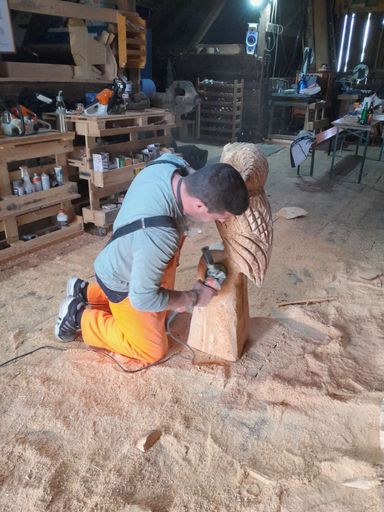 Kursteilnehmer kniet auf dem Boden und bearbeitet eine Holzeule mit einem Winkelschleifer für die Feindetails.
