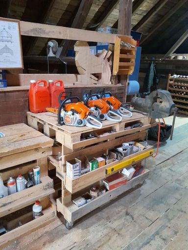 Mehrere orangene Stihl-Kettensägen stehen aufgereiht auf einer Holzpalette in der Werkstatt bereit für Kursteilnehmer