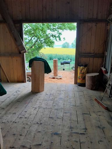 Blick aus dem Scheunentor der Werkstatt von Kettensägenkunst Sachsen auf grüne Felder und Natur im Erzgebirge